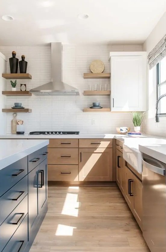 a modern farmhouse kitchen with light-stained cabinets, a navy kitchen island, white stone countertops and a skinny tile backsplash, black handles