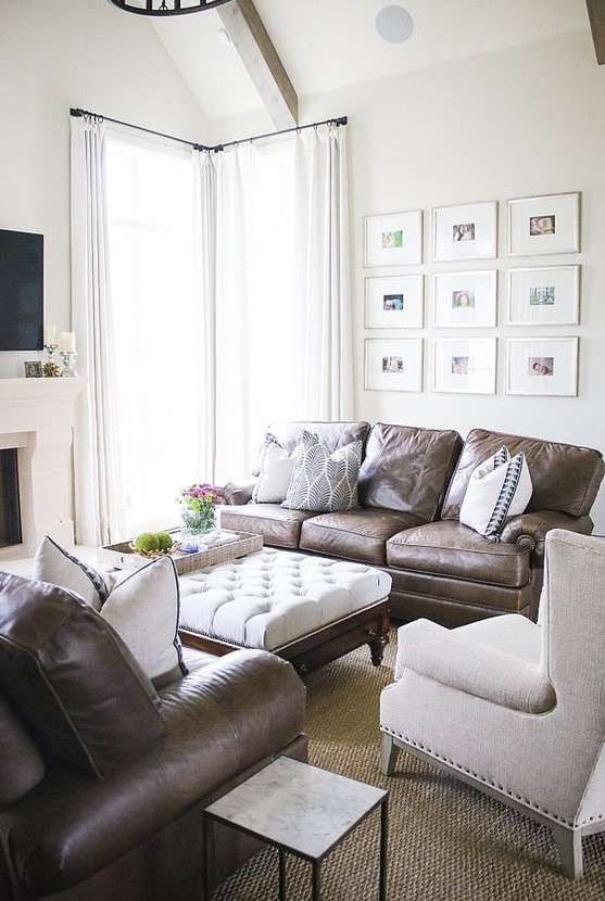 a modern farmhouse living room with a built-in fireplace, brown leather sofas, a neutral chair and a white ottoman, a grid gallery wall