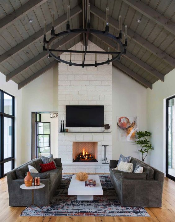 a modern farmhouse living room with a fireplace clad with stone, grey sofas, a coffee table, rug and some decor is cool