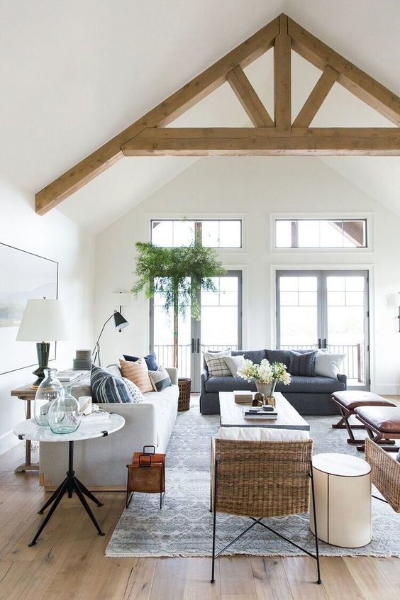 a modern farmhouse living room with a grey and light grey sofa, printed pillows, stools, a coffee table, woven chairs and some tables