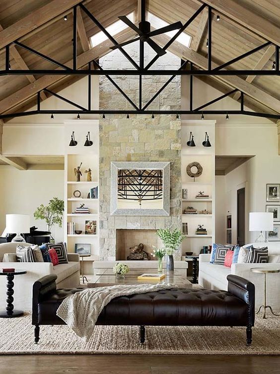 a modern farmhouse living room with a stone clad fireplace, neutral sofas, a dark leather daybed, coffee tables and a skylight