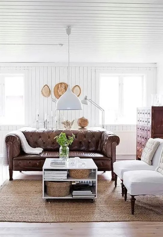 a modern farmhouse living room with white beadboard walls, vintage furniture and a brown leather Chesterfield