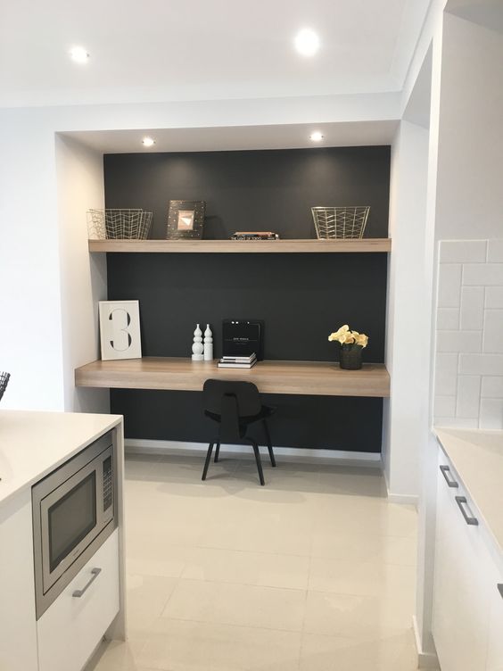 a modern home office nook in a niche with a built-in desk and a shelf, a black chair, some wire baskets and lovely decor