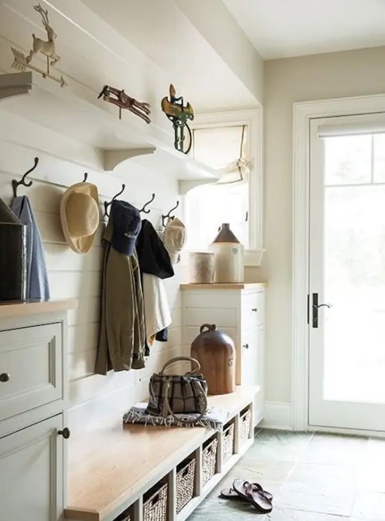 a neutral farmhouse entryway clad with white wooden planks, a built-in bench with woven boxes and much natural light