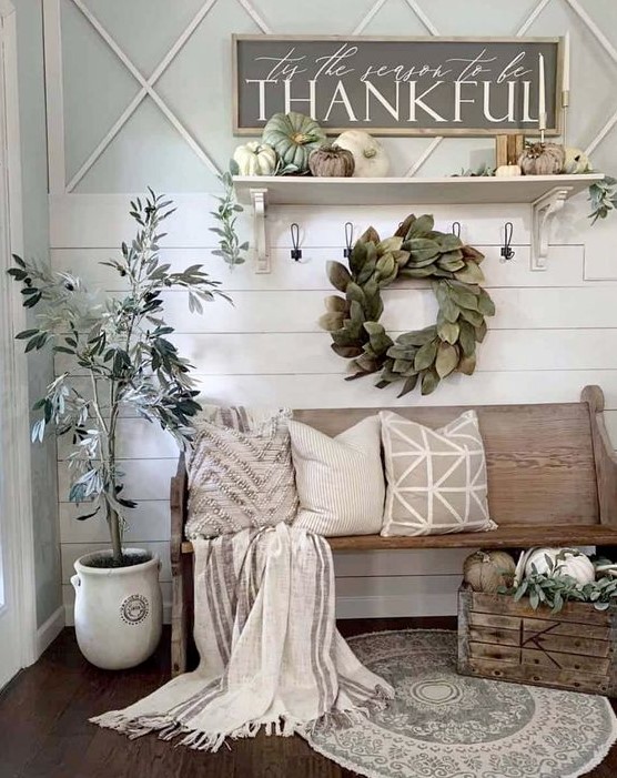 a neutral farmhouse entryway with a leaf wreath, a potted tree, faux pumpkins, candles and neutral textiles