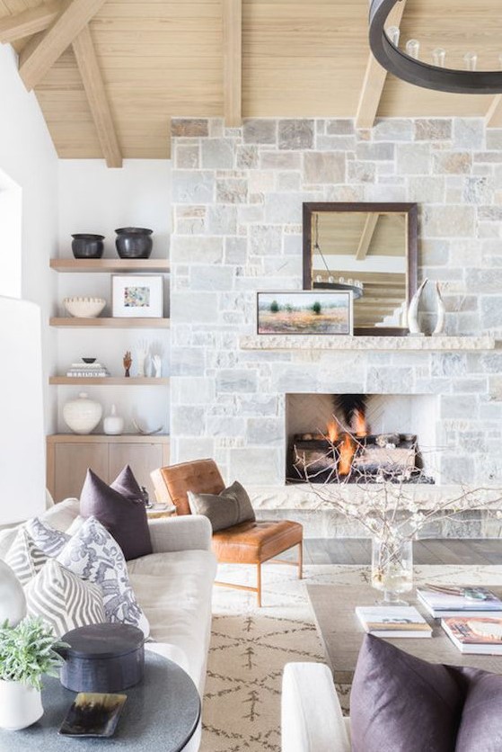 a neutral farmhouse living room with a stone fireplace, a wooden mantel, artworks and a mirror that becomes a centerpiece here