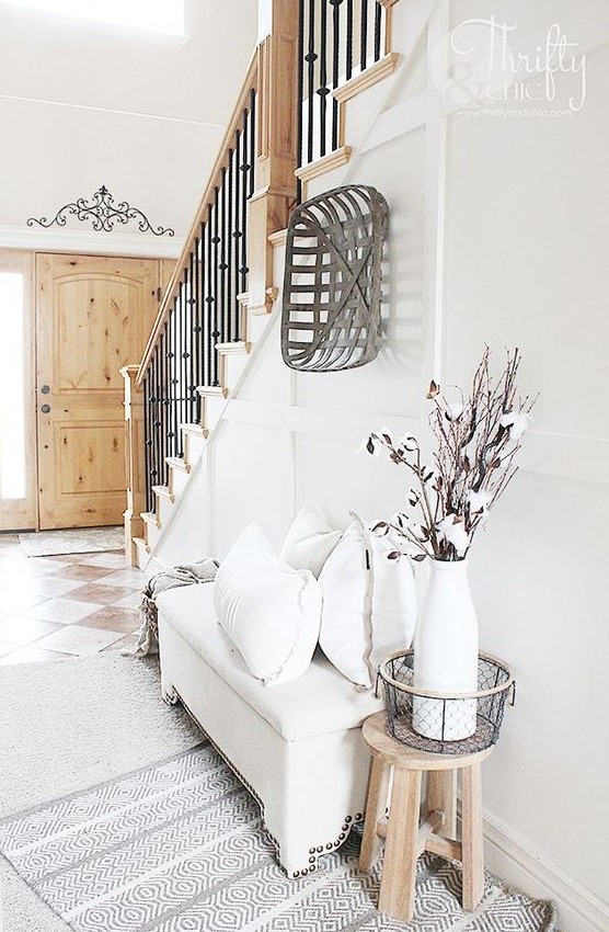 a neutral modern farmhouse entryway with a white upholstered bench, a wooden basket and some cotton branches in a vase