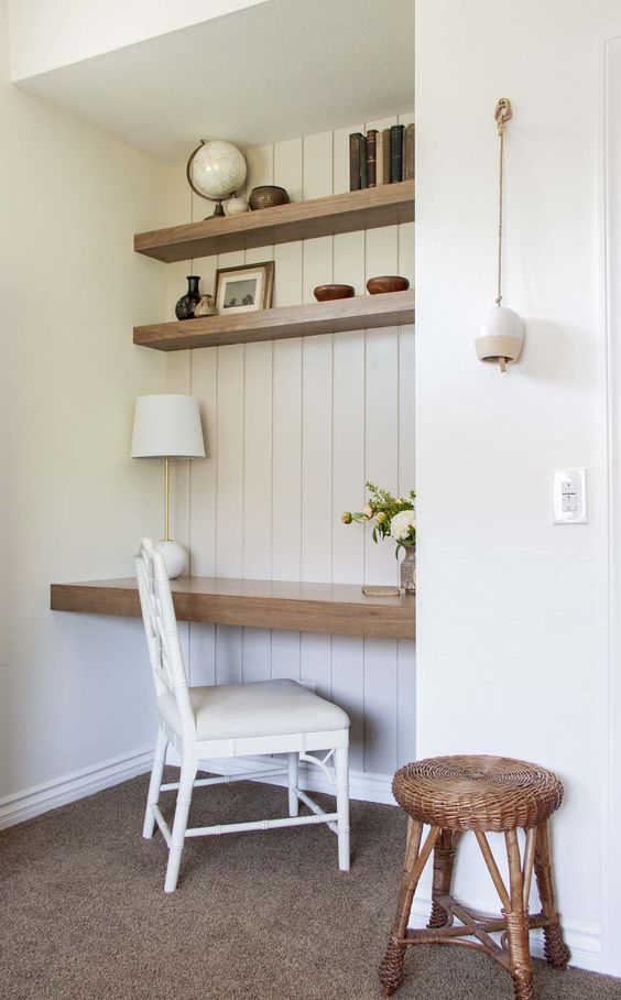 a neutral niche clad with white shiplap, stained shelves and a desk, books, vintage decor and vases, a table lamp