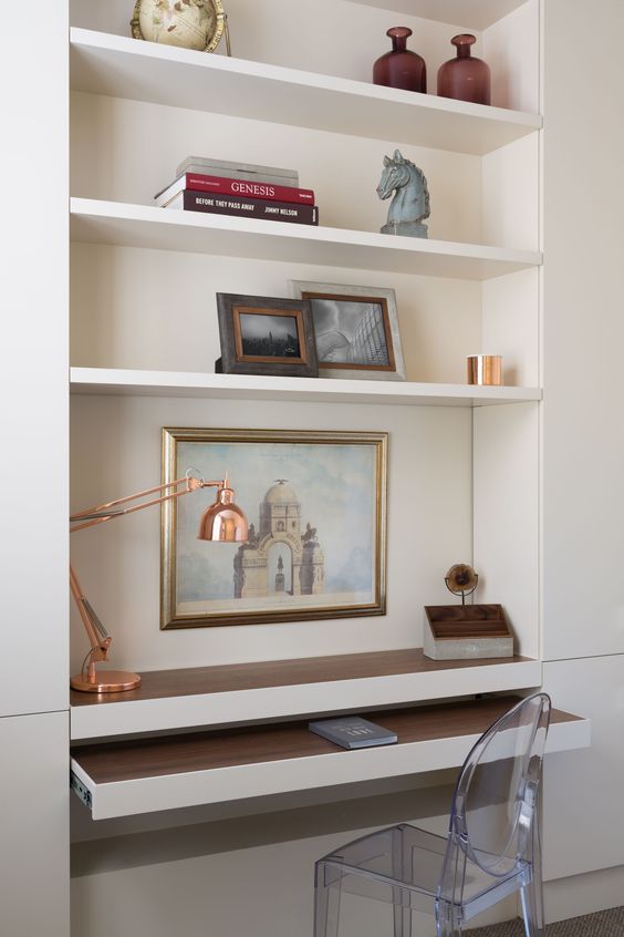 a niche with built-in shelves and a desk plus a retracting part, books, artwork, vases and a copper table lamp