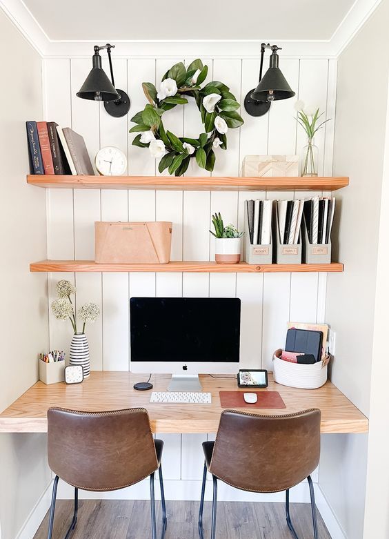 a niche with shiplap, built-in shelves, a desk, potted greenery, black sconces, books and brown leather chairs