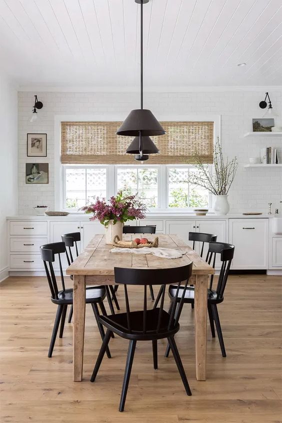 a pretty modern farmhouse dining space with white cabinetry, a stained dining table and black chairs, black pendant lamps and some art