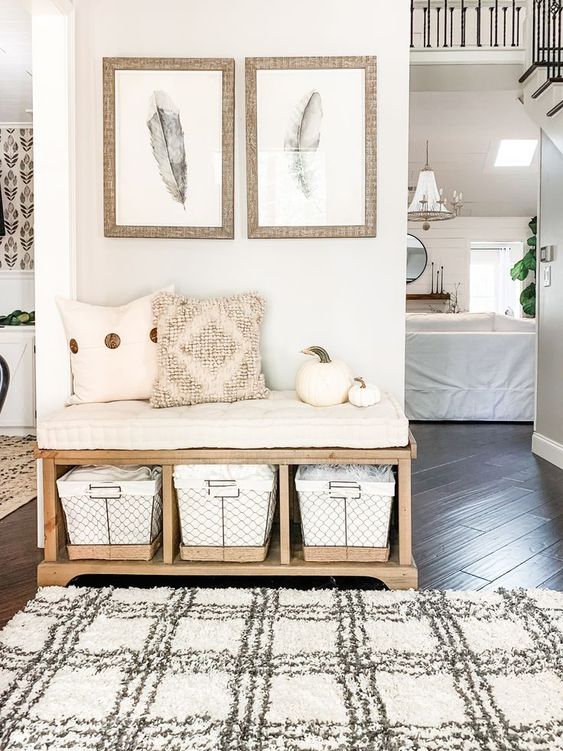 a pretty modern farmhouse entryway with a wooden bench and baskets, some pillows and pumpkins and a bit of art