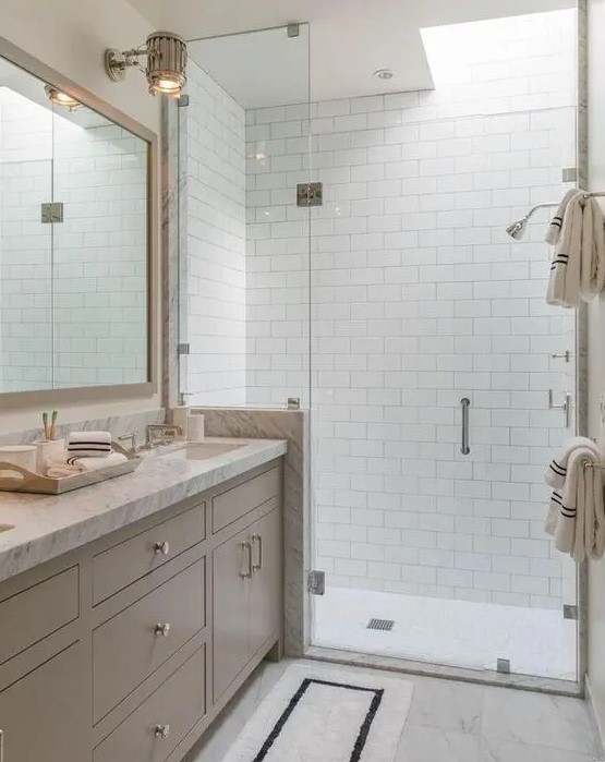 a pretty neutral bathroom clad with subway tiles, with a greige vanity with a white stone countertop and a skylight over the shower