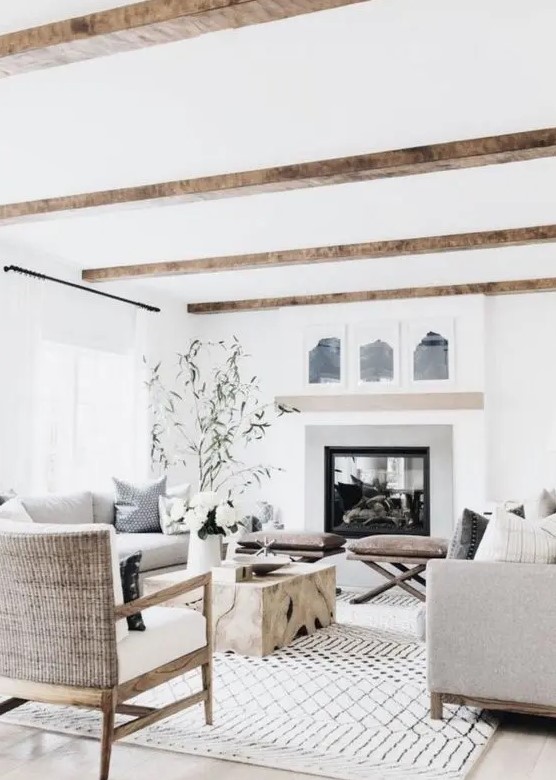 a refined modern country living room with a large fireplace, wooden beams, comfy furniture, a low wooden table and leather stools