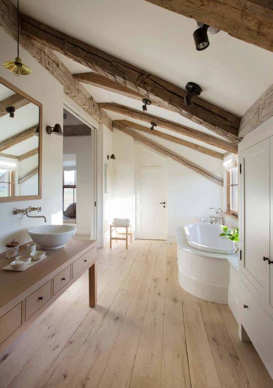 a refined modern farmhouse bathroom with a timber table vanity, wooden beams on the ceiling, a tub, a large wardrobe