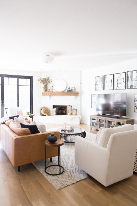 a serene modern farmhouse living room with a fireplace, a gallery wall, a TV, a leather sofa and neutral chairs