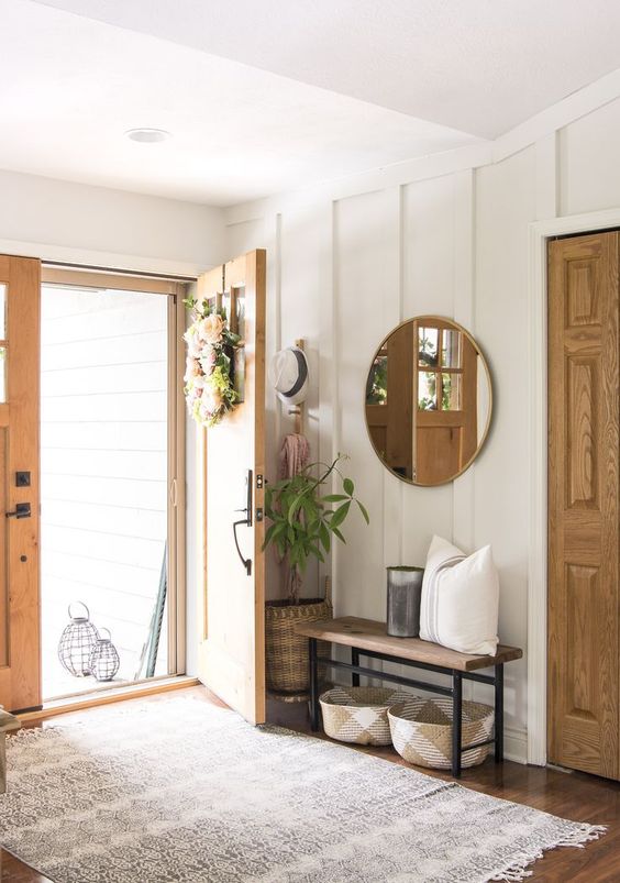 a simple and stylish modern farmhouse entryway with a bench, some baskets, a round mirror and some greenery