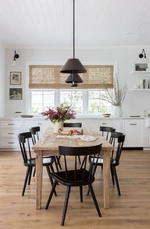 a simple modern farmhouse dining space with a stained wooden table, vintage black chairs, modern black pendant lamps is cool