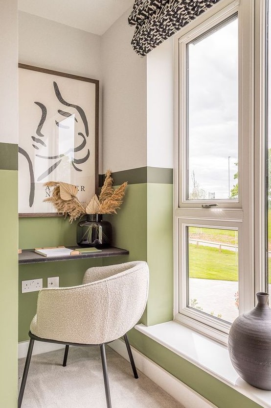 a small and bright home office nook by the window, with a built-in desk, a neutral chair, a statement artwork and some dried leaves in a vase