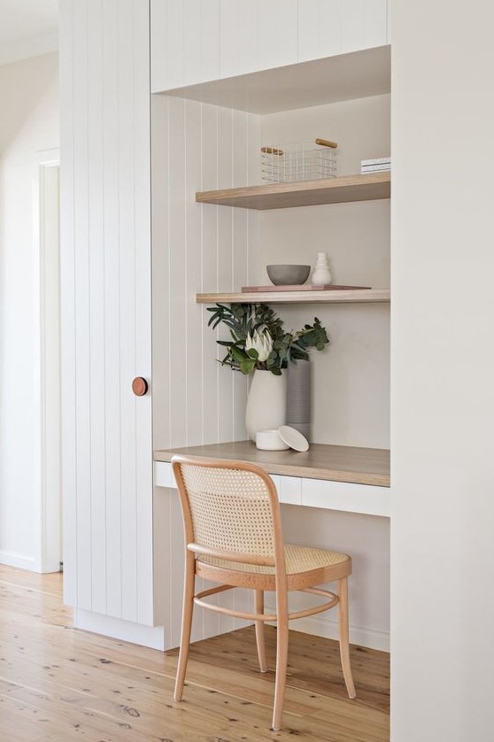 a small and clean working nook with a couple of built-in shelves and a desk, a woven chair, potted greenery and decor