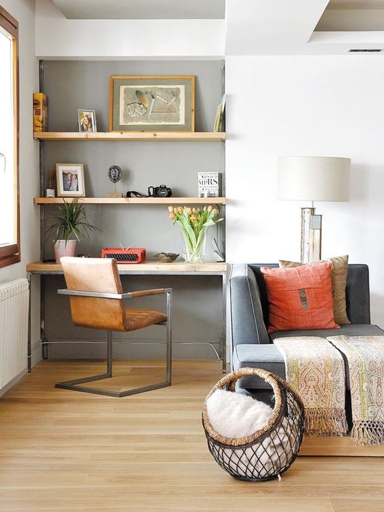 a small and cozy home office nook in the living room, with built-in shelves and a desk, a brown leather chair and blooms and art