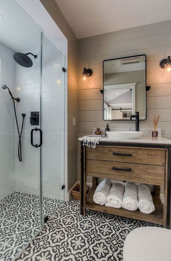 a small farmhouse bathroom with neutral tiles, patterned ones on the floor, a wooden vanity and black fixtures here and there