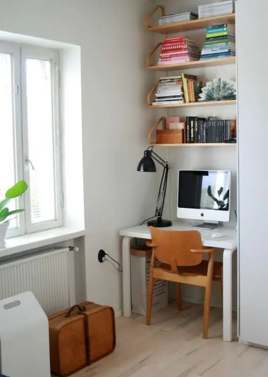 a small nook by the window with a white desk and some suspended shelves, a plywood chair and a black table lamp