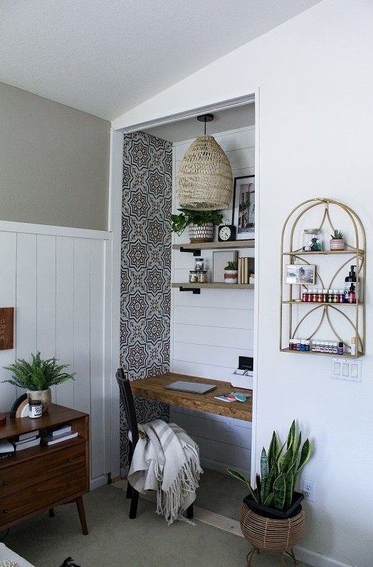 a small working nook in a bedroom, with a built-in desk and shelves, a black chair, a woven pendant lamp and some greenery