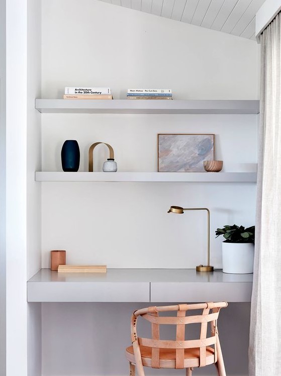 a small working space in a living room, with built-in shelves and a desk with drawers, a woven chair and a small brass lamp