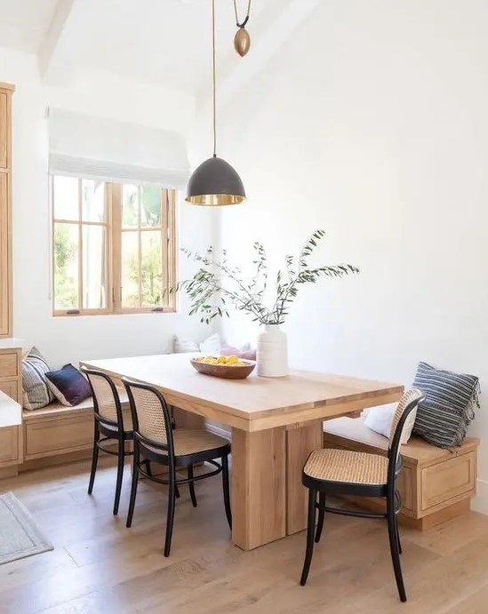 a stylish modern dining space with a stained built-in bench, a stained table and black wooden and cane chairs plus printed pillows