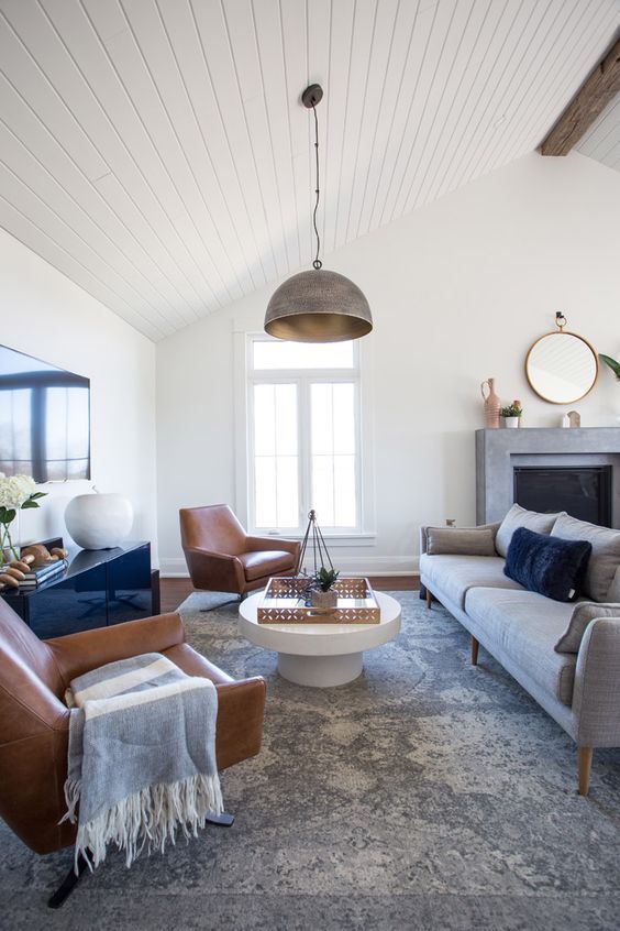 a stylish modern farmhouse living room with a fireplace, a grey sofa, leather chairs, a glossy sideboard and a coffee table