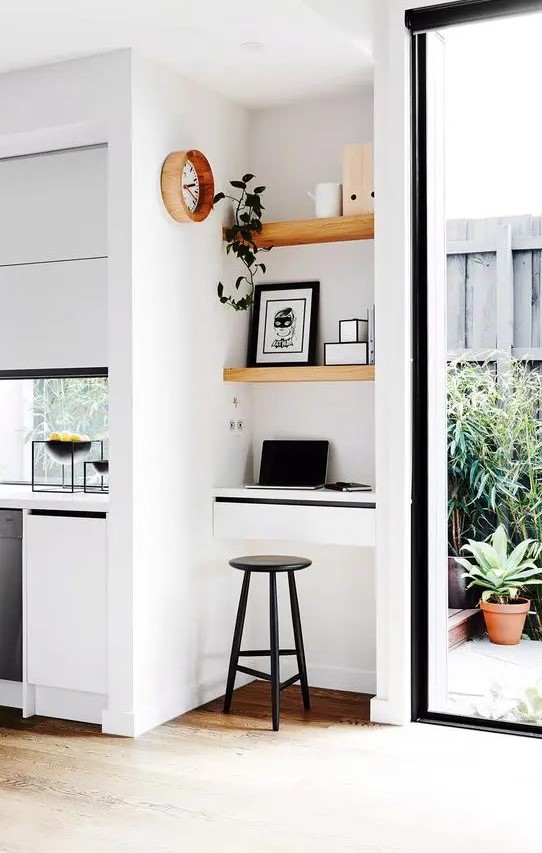 a super tiny working nook with built-in shelves and a small desk with drawers, a black stool, artworks and a potted plant