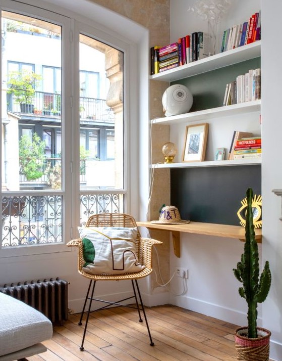 a tiny home office nook in the living room, with built-in shelves and a desk, a woven chair and a potted cactus