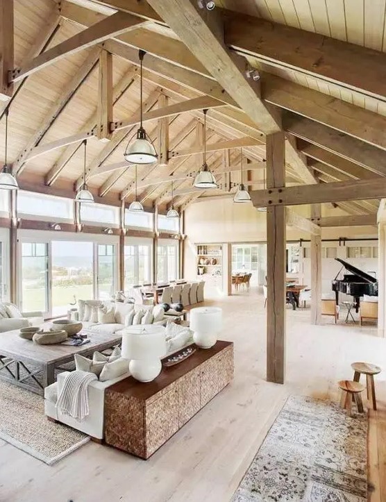 a welcoming barn living room with a stained wooden ceiling and beams and pillars, neutral seating furniture, wooden furniture items and a piano