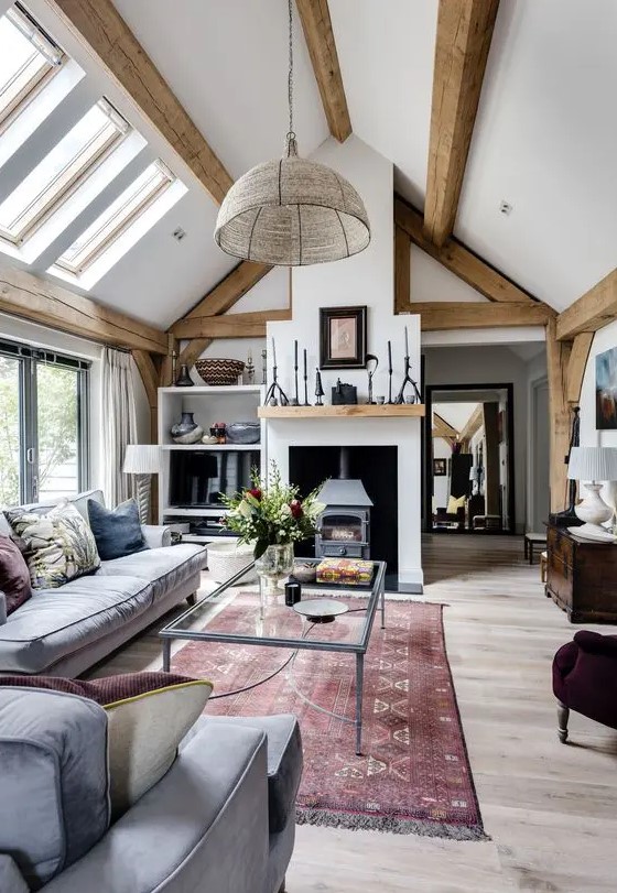 a welcoming barn living room with wooden beams, a vintage hearth, grey seating furniture, a glass sofa, various accessories