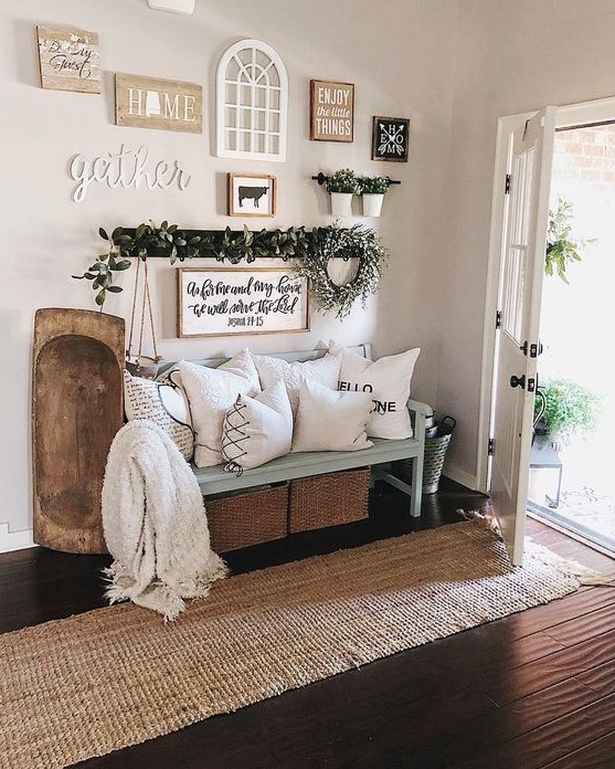 a welcoming entryway with a jute rug, a blue bench, printed pillows, a dough bowl and a large gallery wall with various pieces