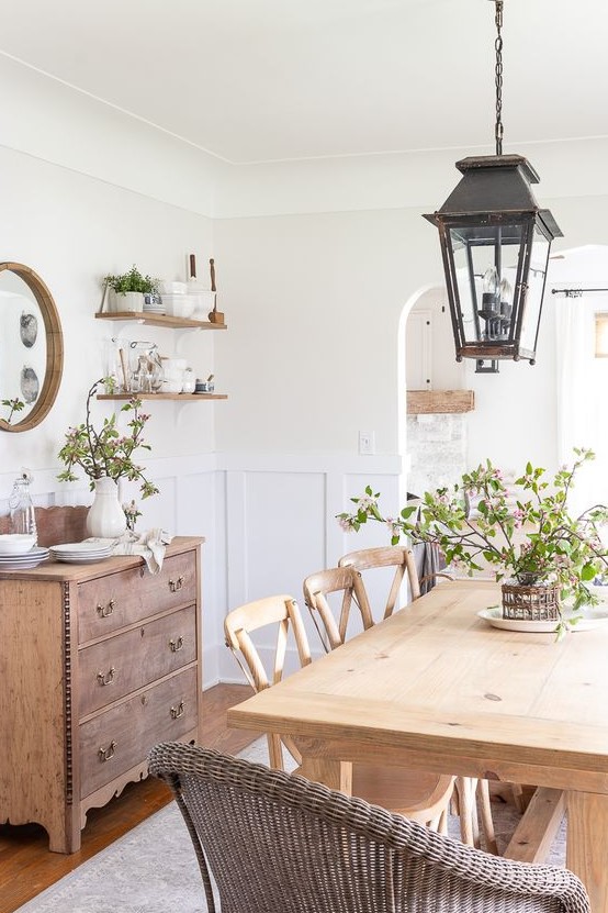 a welcoming farmhouse dining room with a light-stained table and chairs, wicker chairs, a stained credenza, metal lanterns and greenery