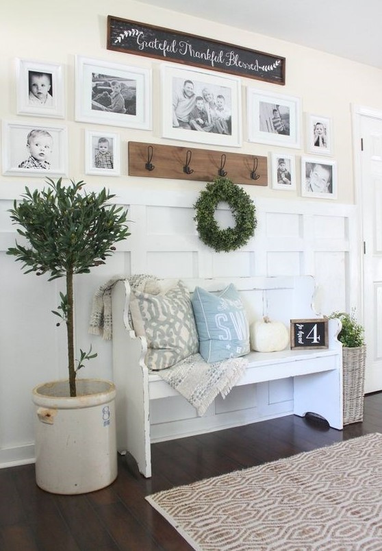 a welcoming farmhouse entryway with a gallery wall of family pics, a white bench with pillows, potted plants and a rack