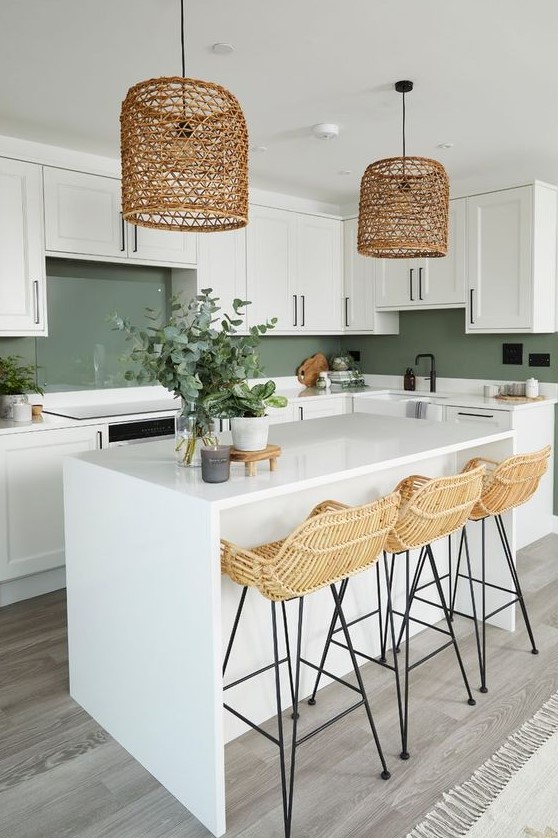 a welcoming farmhouse kitchen with white cabinets and a green backsplash, stone countertops, a white kitchen island, rattan stools and woven lamps