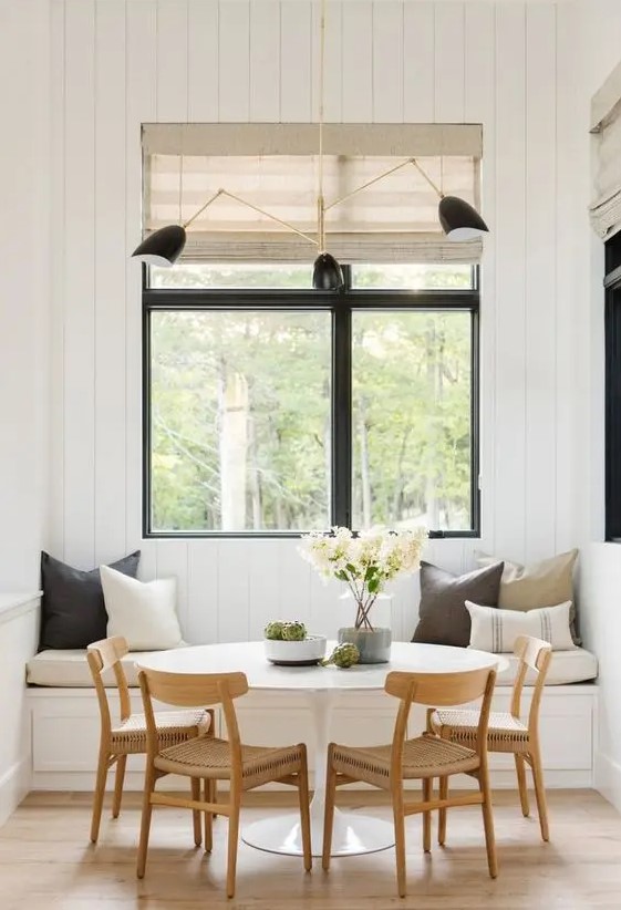 a welcoming modern farmhouse dining space with a built-in bench, a round table, woven chairs, touches of black and woven shades