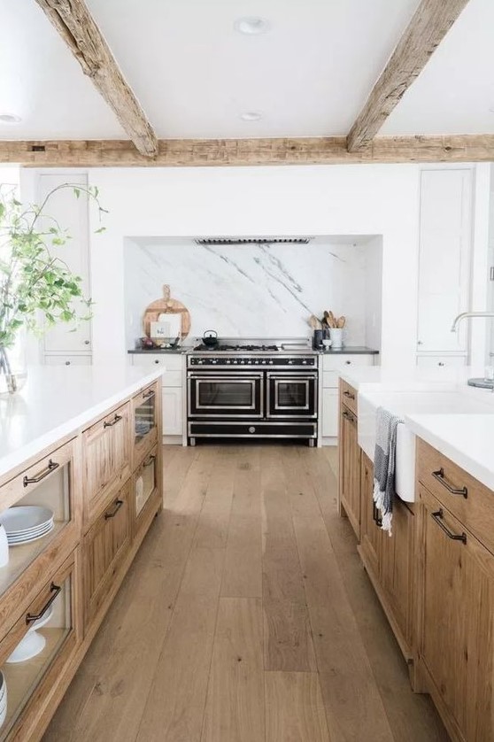 a welcoming modern farmhouse kitchen with white and stained cabinets, white stone countertops, wooden beams and a black cooker