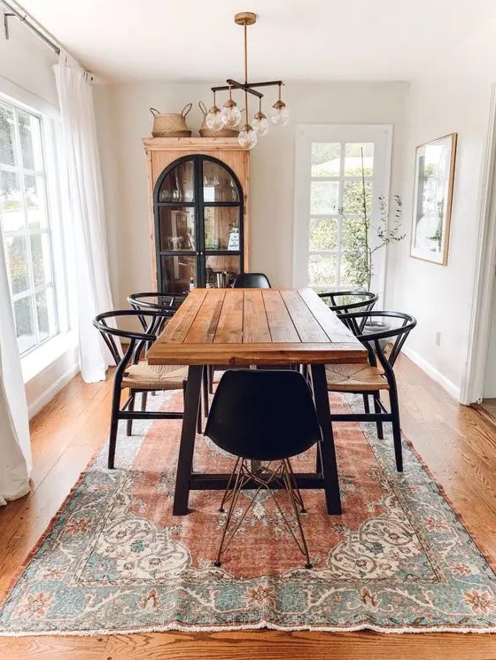 a welcoming rustic dining space with a dining table with a stained tabletop, black woven chairs, a chic chandelier and a vintage buffet