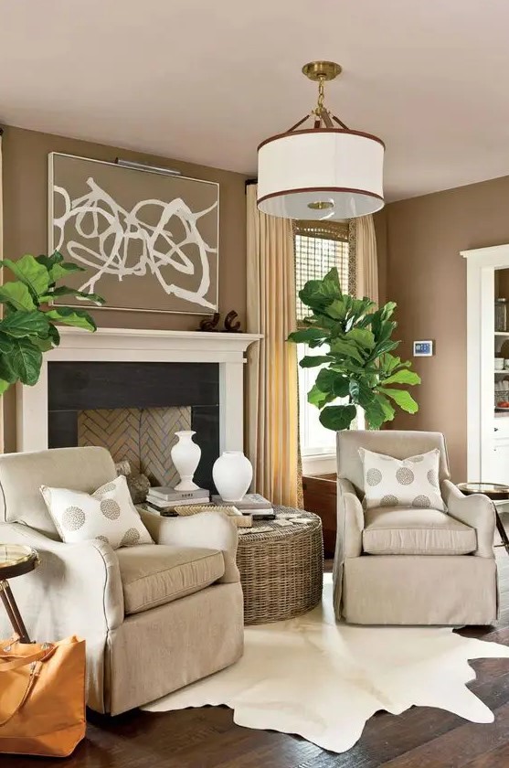 a welcoming taupe living room with a vintage-styled fireplace, tan chairs, a woven coffee table, statement potted plants and polka dot pillows