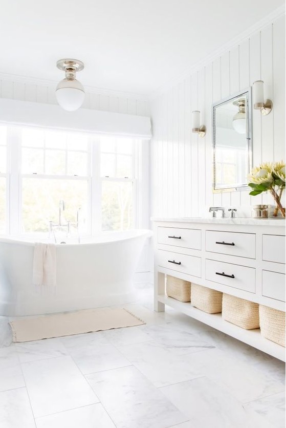 a white bathroom with shiplap walls, white marble tiles on the floor and a tub by the window looks very airy