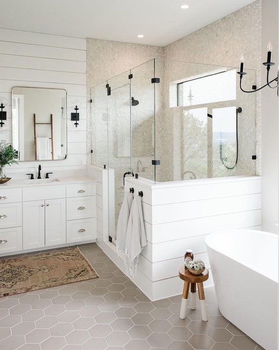 a white farmhouse bathroom with plank walls, grey hex tiles, an oval tub, a vintage vanity and touches of black