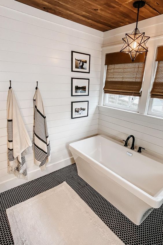 a white modern farmhouse bathroom with shiplap walls, a tub, windows with shades, a star-shaped pendant lamp and a penny tile floor