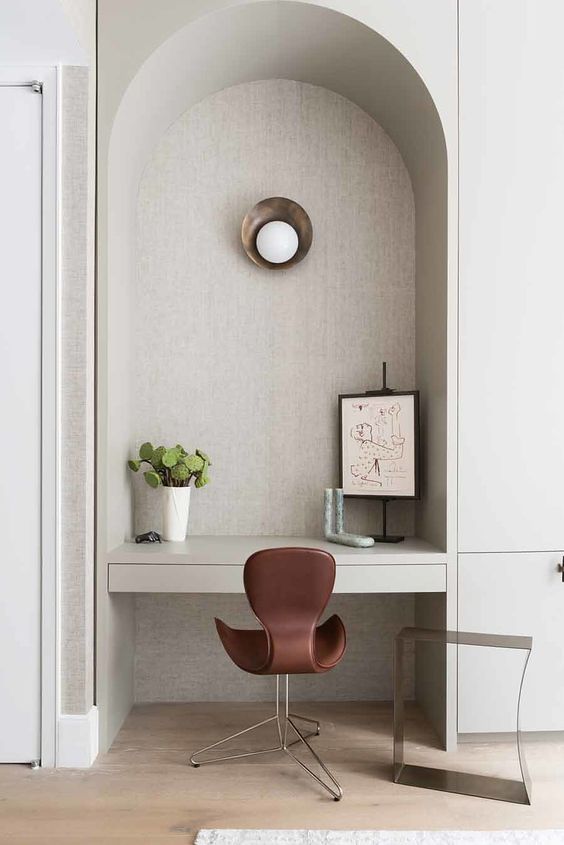 an ached niche with a built-in desk, some art, a sconce and a burgundy chair is adorable and chic