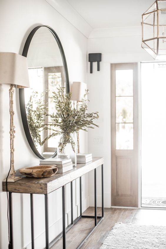 an airy modern farmhouse entryway with a large mirror, a console table, some greenery and table lamps and coffee table books