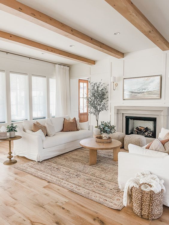 an airy modern farmhouse living room with wooden beams, a fireplace, white sofas and a wooden coffee table plus some baskets