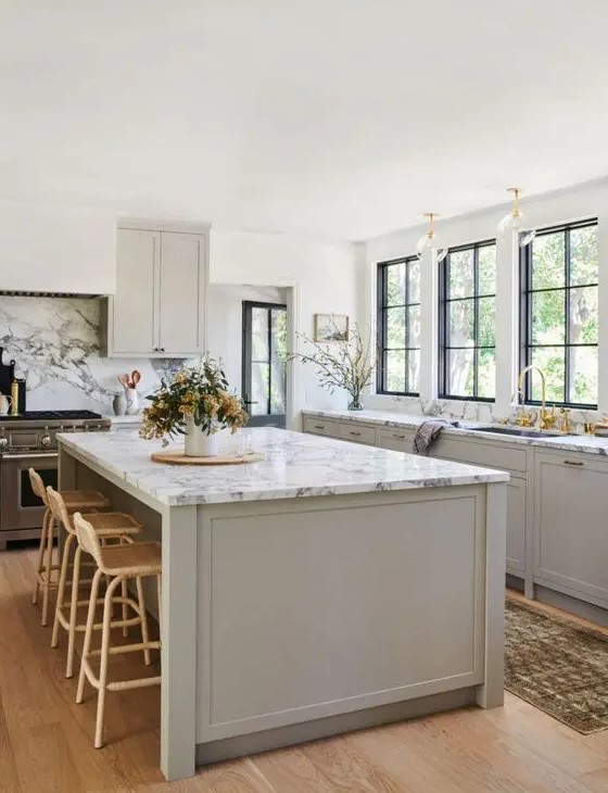 an inspiring dove grey modern country kitchen with shaker style cabients, white marble countertops, gold touches and rattan stools